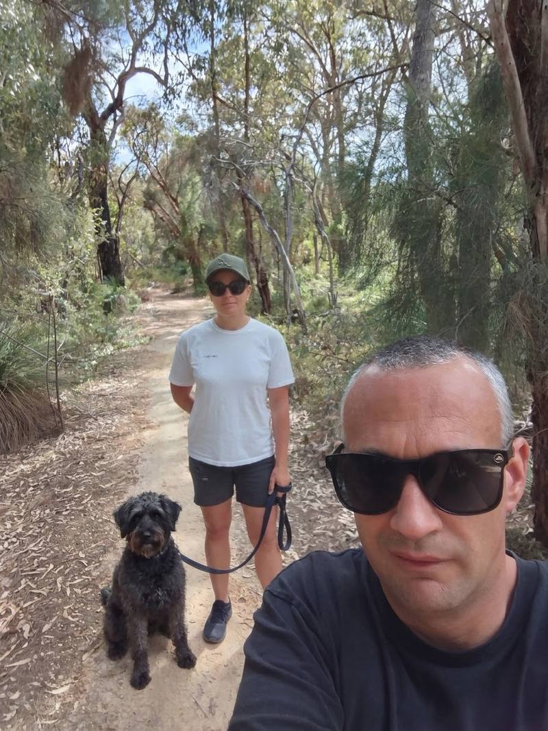 Two pet sitters out walking a black curly-haired dog on a bush trail