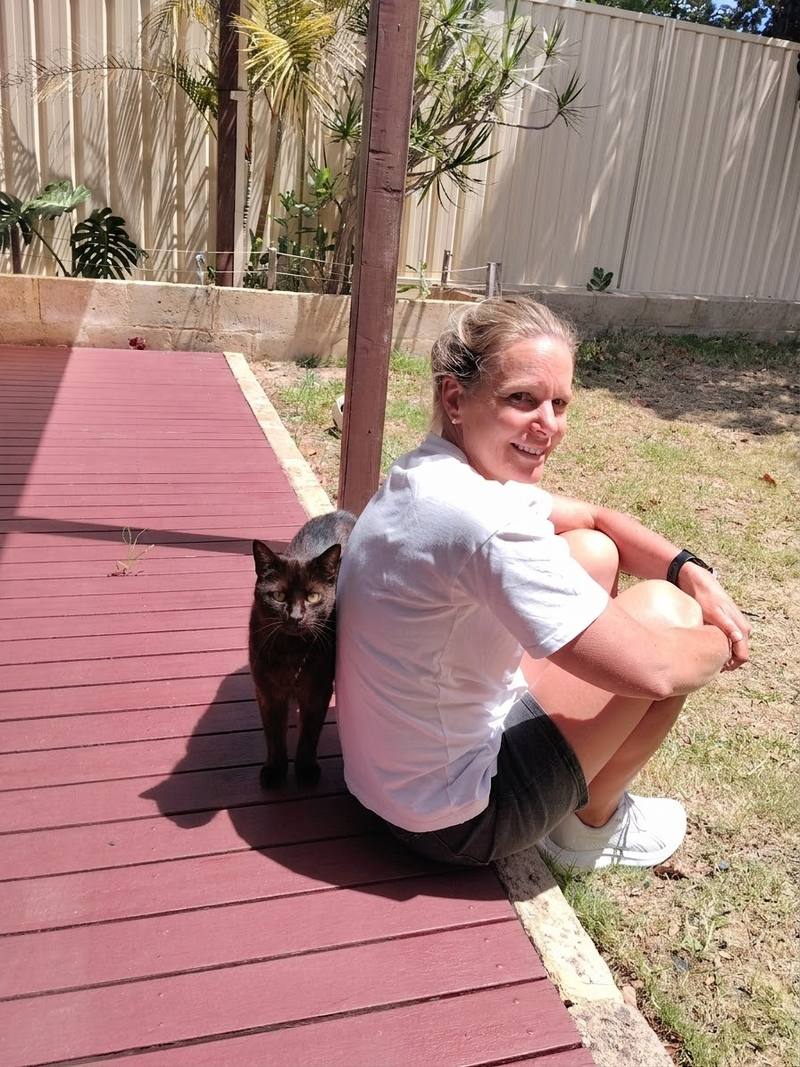 A black cat leaning against a pet sitter relaxing on a backyard deck